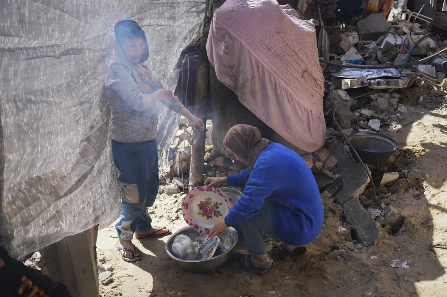 Rawya Tamboura and her son Yazan wash dishes next to their home, which was struck by an Israeli airstrike on Oct. 20, 2023, in Beit Lahiya, northern Gaza Strip, Friday, Feb. 21, 2025. (AP)