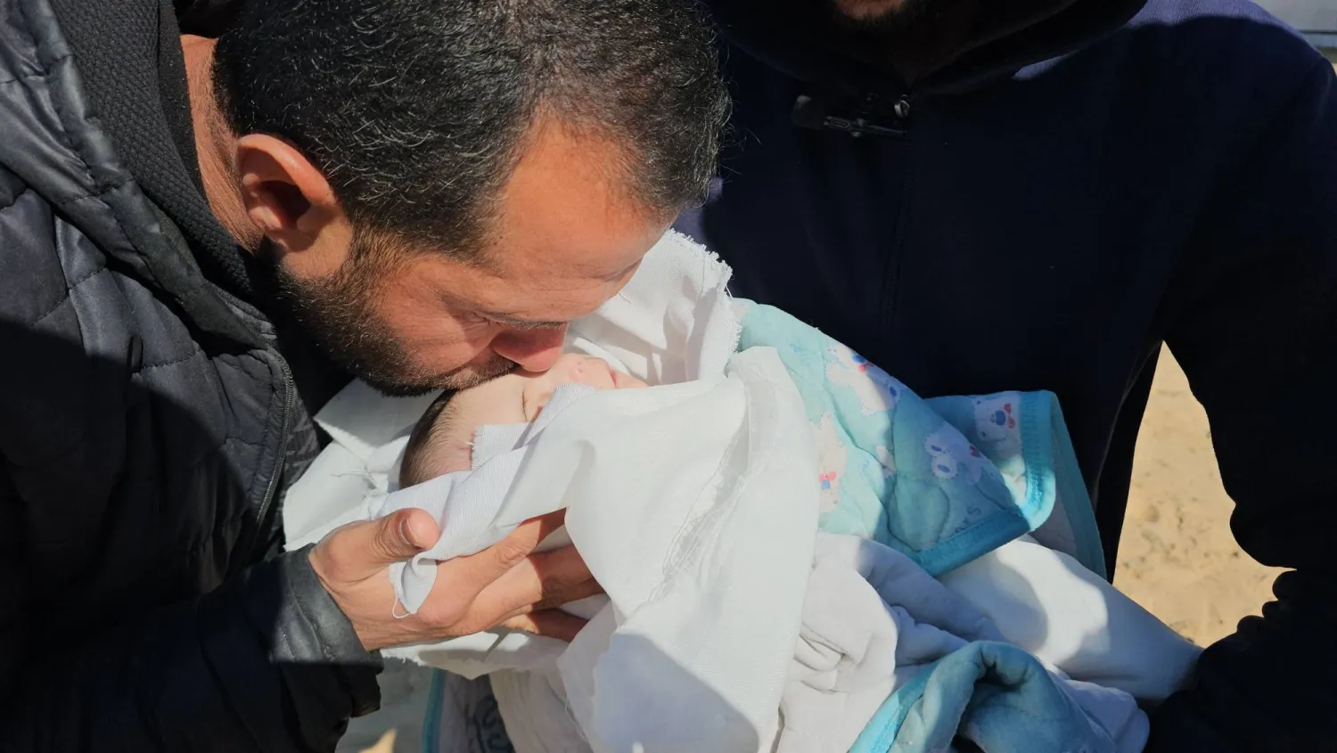 الرضيعة الفلسطينية شام الشنباري التي توفيت الثلاثاء من جراء البرد القارس في غزة يقبلها أحد أقاربها قبل دفنها (الشرق الأوسط)