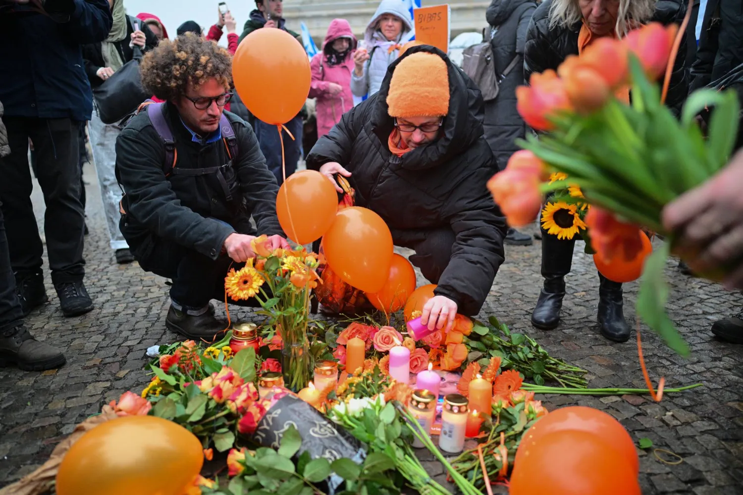 أشخاص يضعون بالونات برتقالية وشموعاً أمام بوابة براندنبورغ خلال مراسم تذكارية لإحياء ذكرى أفراد عائلة بيباس في إسرائيل (د.ب.أ)