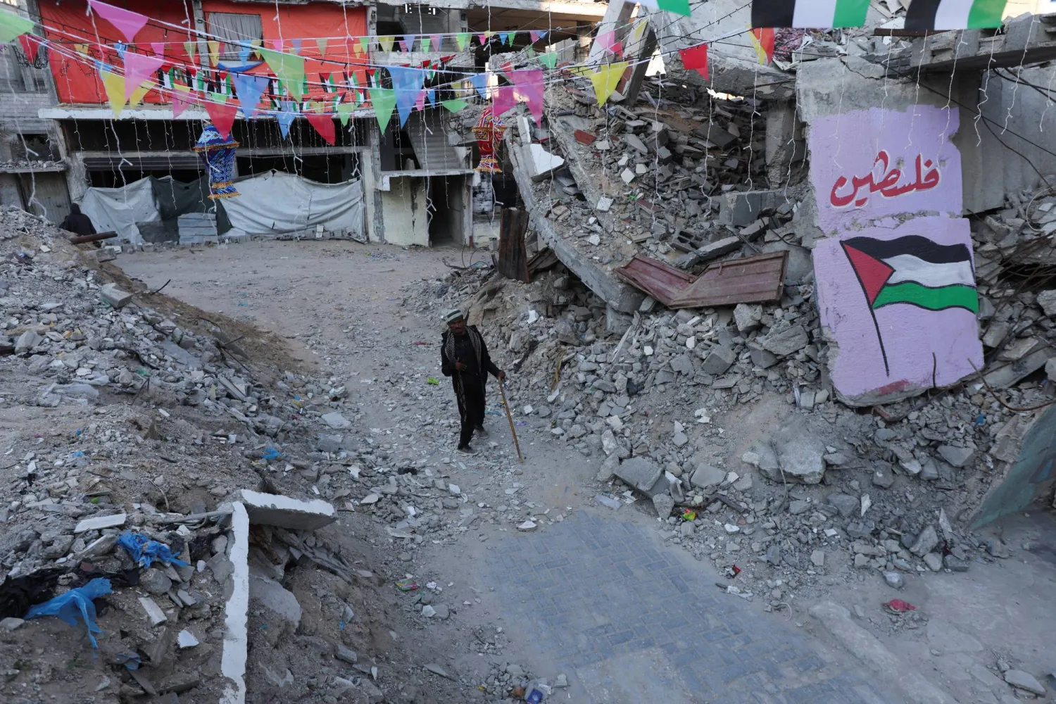 A Palestinian walks past graffiti and the rubble of buildings, ahead of the holy fasting month of Ramadan, amid a ceasefire between Israel and Hamas, in Khan Younis, in the southern Gaza Strip, February 27, 2025. REUTERS/Ramadan Abed