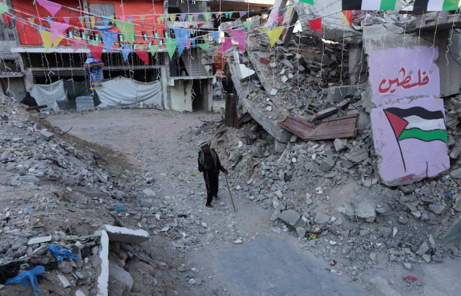 A Palestinian walks past graffiti and the rubble of buildings, ahead of the holy fasting month of Ramadan, amid a ceasefire between Israel and Hamas, in Khan Younis, in the southern Gaza Strip, February 27, 2025. REUTERS/Ramadan Abed/File Photo 