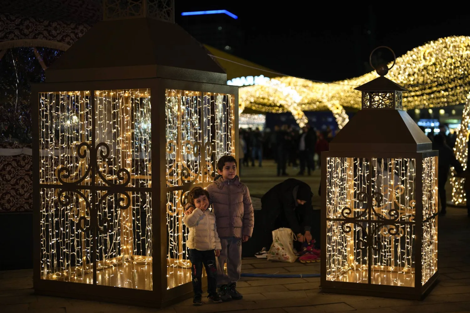 Children pose for a picture next to the lighting decorations in a square on the first day of the Muslim holy month of Ramadan in Istanbul, Türkiye, Saturday, March 1, 2025. (AP Photo/Khalil Hamra)