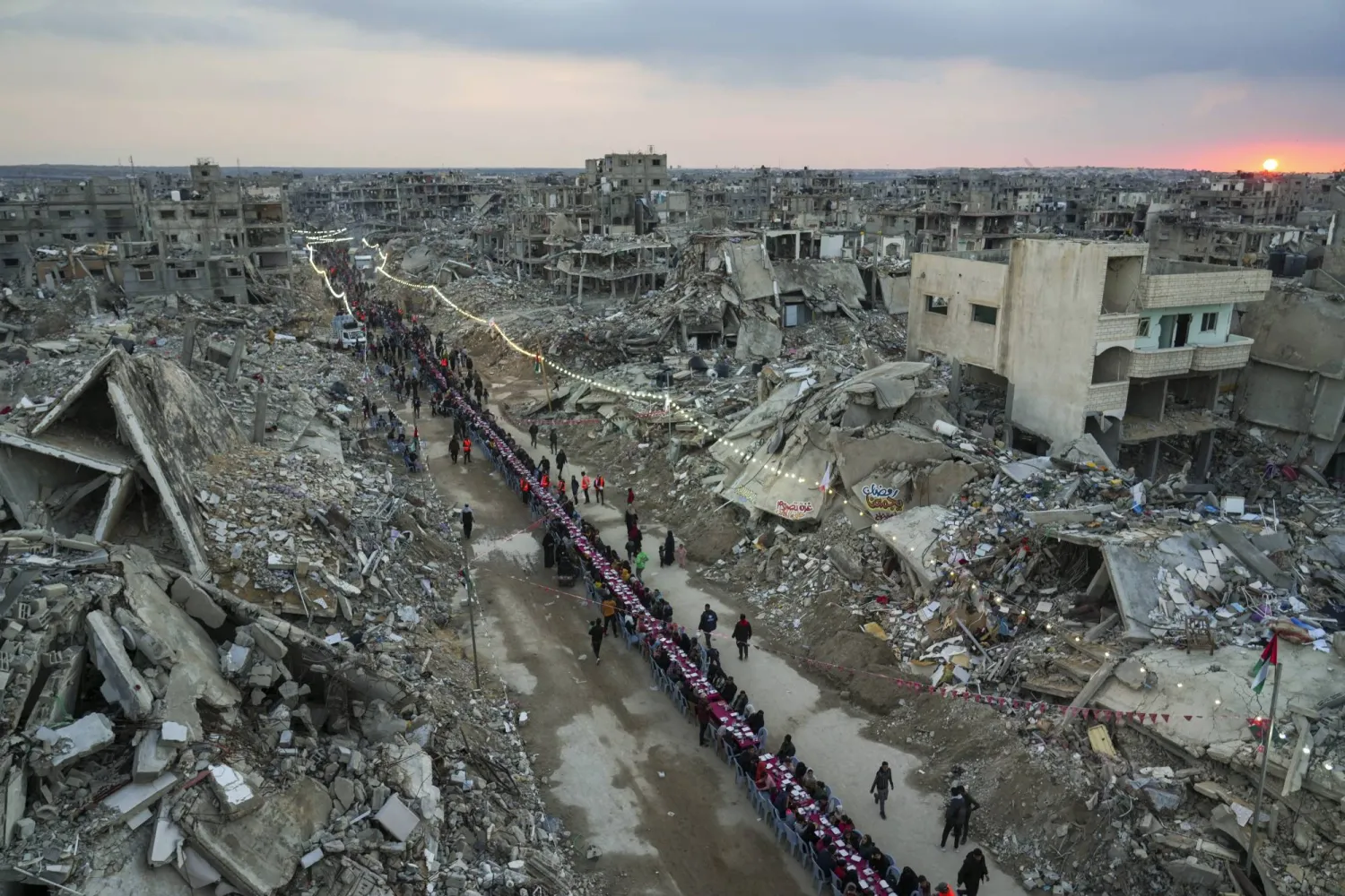 As the sun sets, Palestinians sit at a large table surrounded by the rubble of destroyed homes and buildings as they gather for iftar on the first day of Ramadan in Rafah, southern Gaza Strip,Saturday, March 1, 2025 (AP Photo/Abdel Kareem Hana)