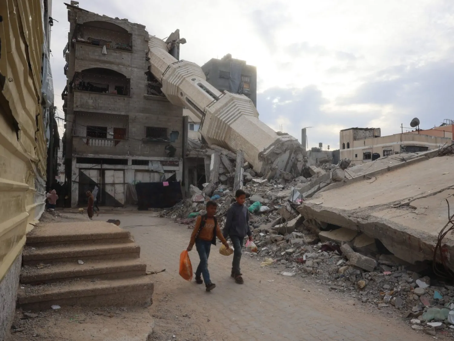 طفلان فلسطينيان يمشيان أمس بين المباني المهدمة في مخيم النصيرات للاجئين في غزة (أ.ف.ب)