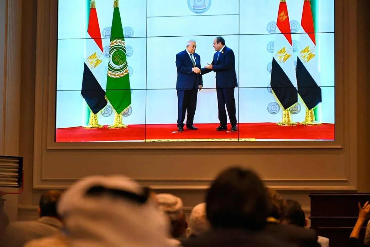 People watch on a big screen as Egypt's President Abdel Fattah al-Sisi (R) welcomes Palestinian President Mahmoud Abbas ahead of an Arab League summit on Gaza on March 4, 2025. (AFP) 