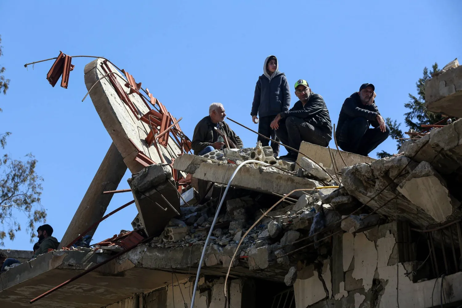 لبنانيون يقفون على الركام في بلدة عيترون جنوب لبنان أثناء تشييع العشرات (د.ب.أ)