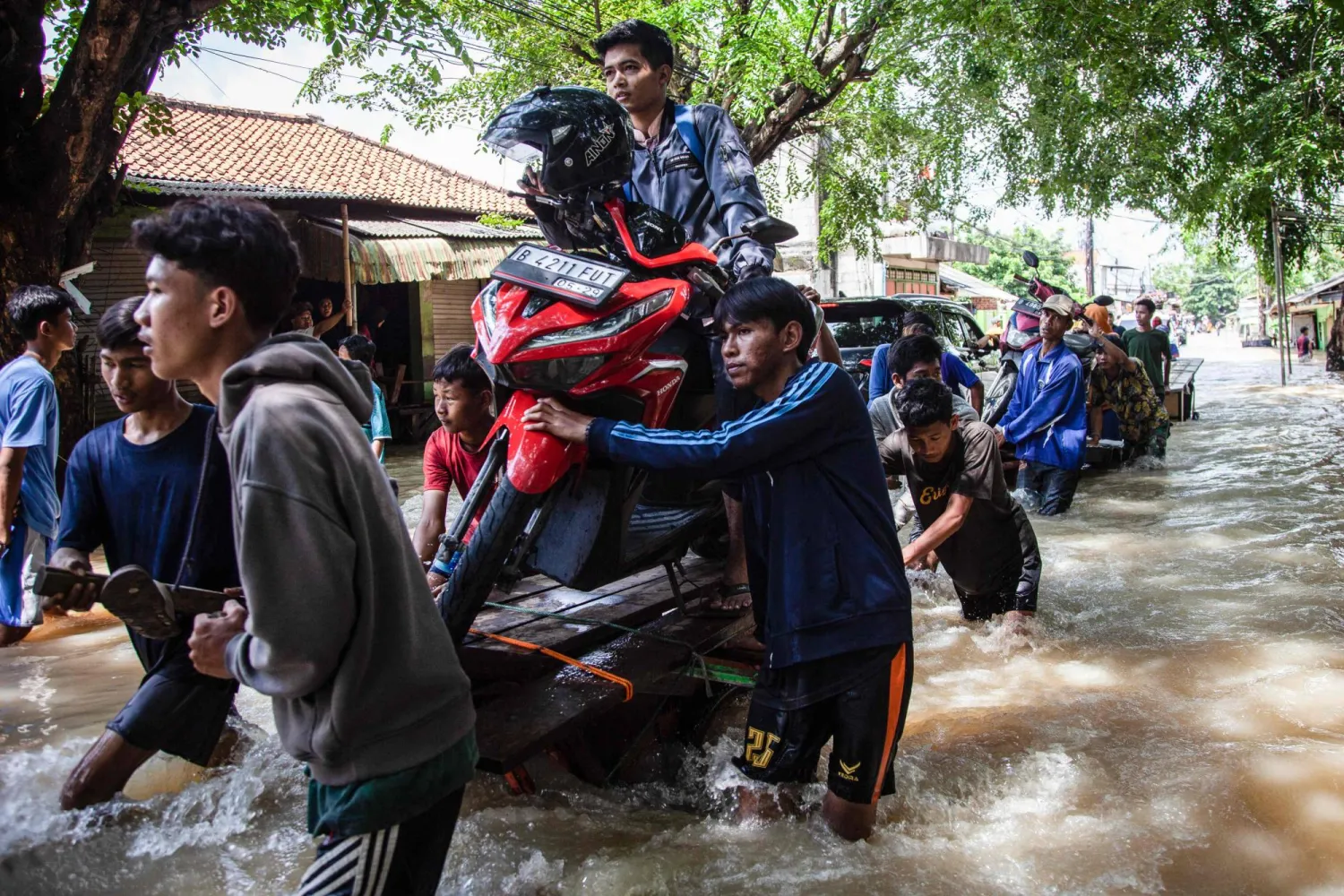 People move a scooter on a cart through a flooded area after some rivers overflowed following heavy rain in Bekasi, a suburb of Jakarta, on March 5, 2025. (Photo by Aditya Irawan / AFP)