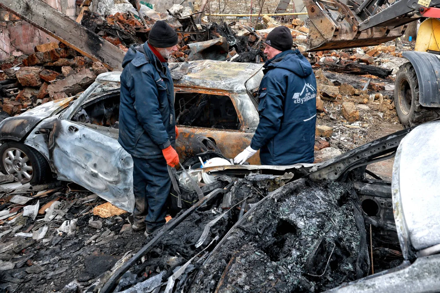 يقف عمال المرافق العامة بجوار السيارات المحترقة نتيجة هجوم بطائرة دون طيار روسية على أوديسا (د.ب.أ)