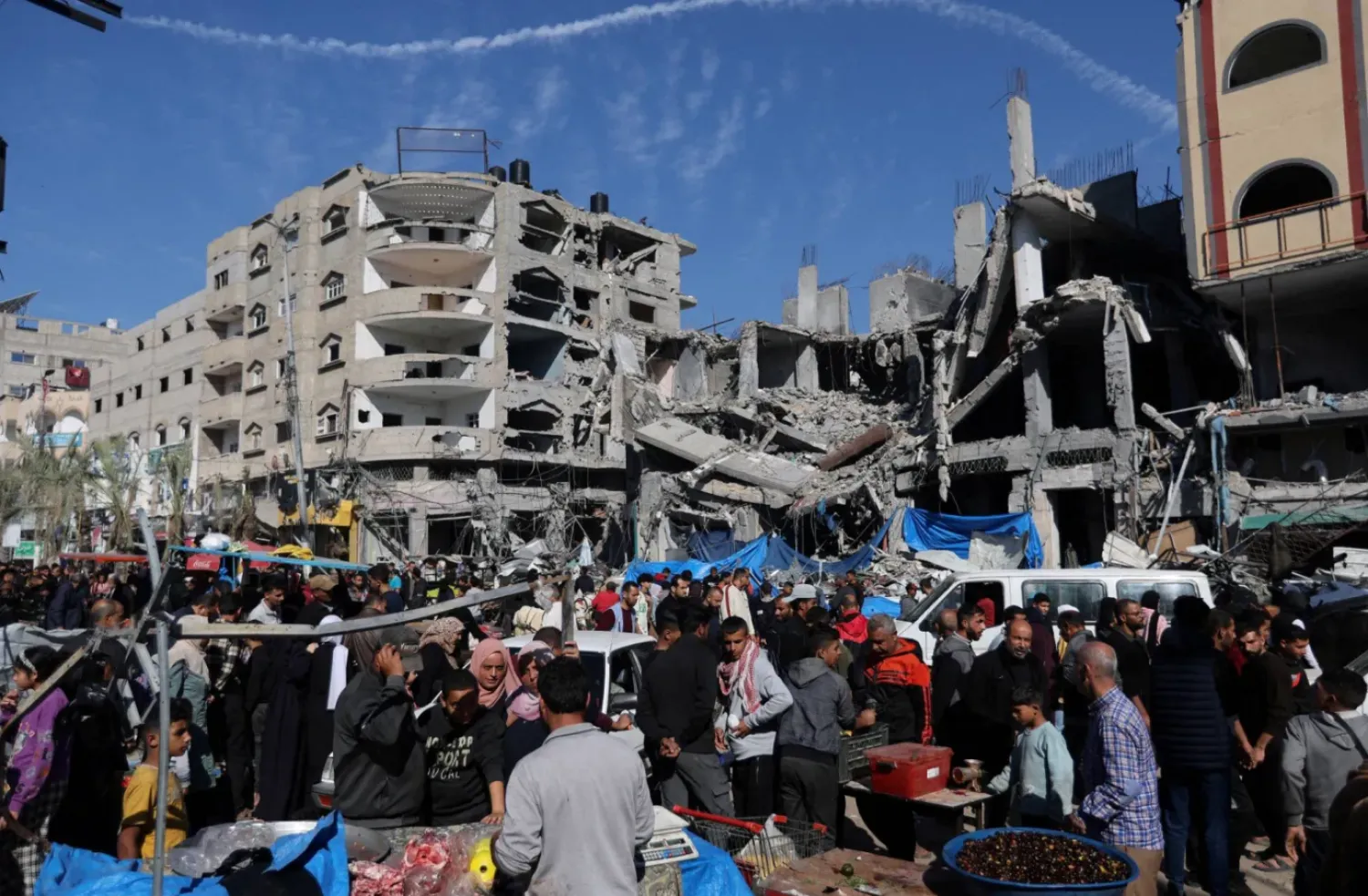 فلسطينيون في سوق أقيمت في الهواء الطلق قرب أنقاض المباني التي دمرتها الضربات الإسرائيلية (رويترز)