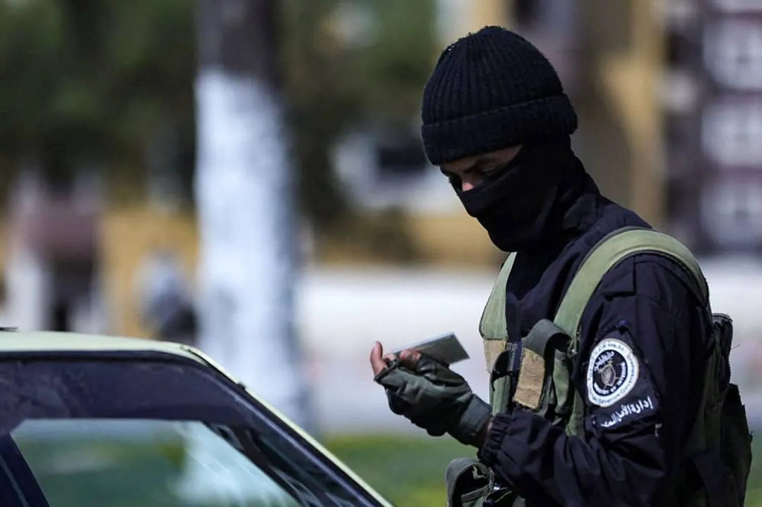 This handout picture released by the official Syrian Arab News Agency (SANA) on March 8, 2025, shows a member of the Syrian forces checking the identity card of a driver at a checkpoint in the coastal city of Latakia. (SANA/AFP)
