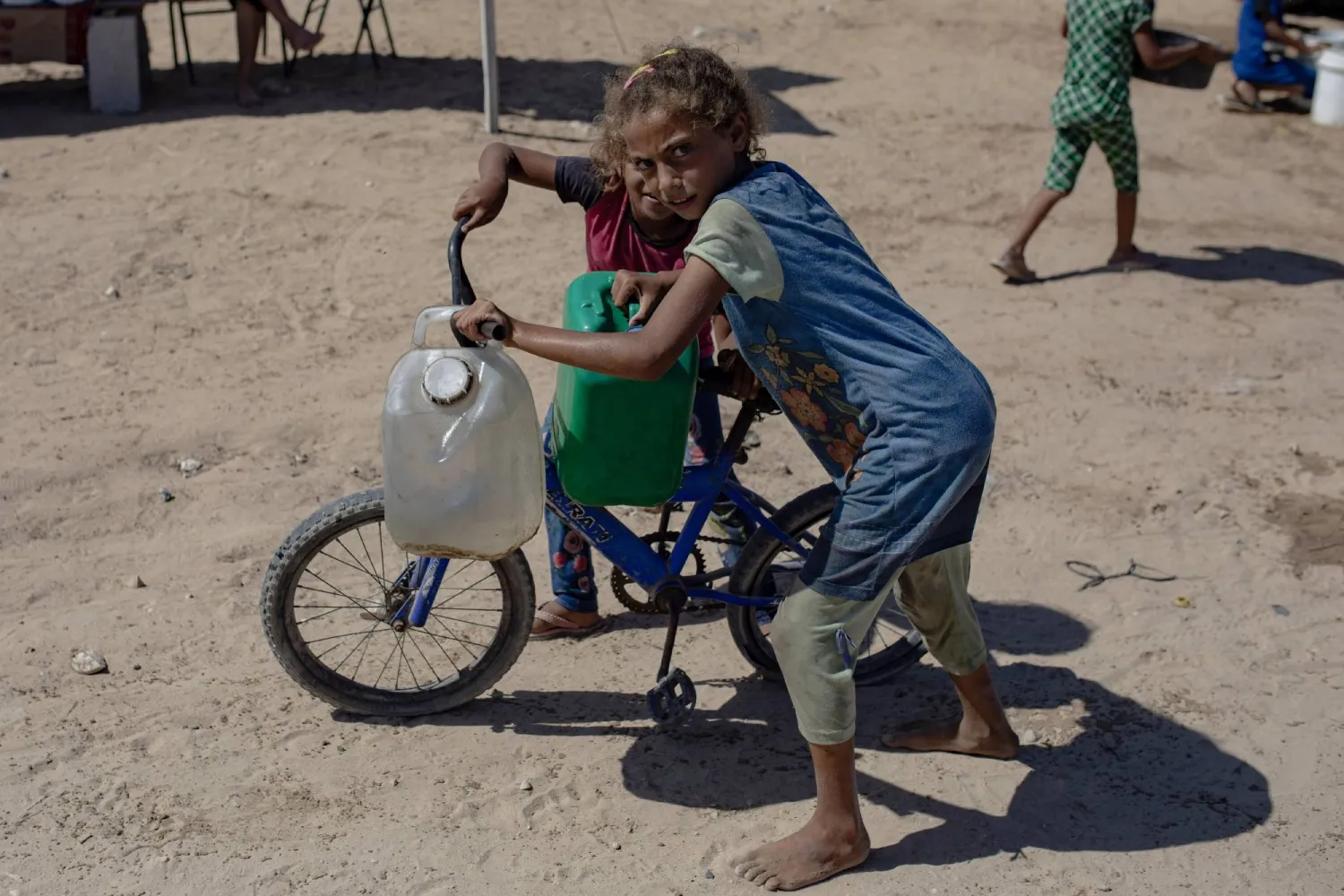 طفلة تحمل الماء على دراجة بينما يجمع الفلسطينيون النازحون مياه الشرب من صهريج مياه في مخيم مؤقت بمخيم خان يونس للاجئين جنوب قطاع غزة (أرشيفية - إ.ب.أ)