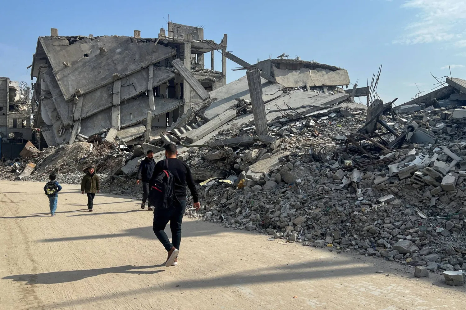 FILE PHOTO: Palestinians walk past the rubble of destroyed houses, amid a ceasefire between Israel and Hamas, in Khan Younis in the southern Gaza Strip, March 6, 2025. REUTERS/Hussam Al-Masri/File Photo