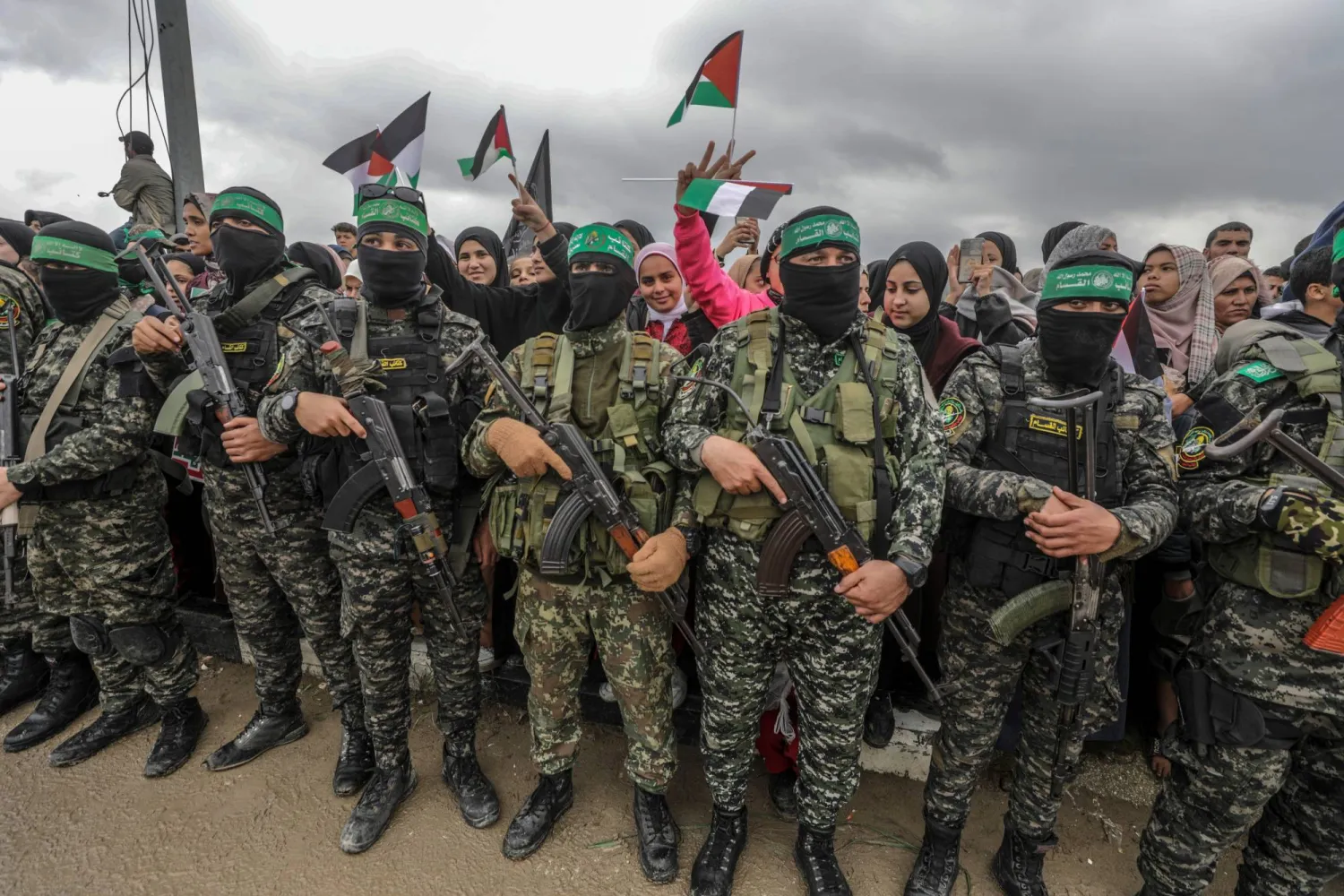 فلسطينيون يقفون خلف مقاتلين مسلحين من كتائب عز الدين القسام التابعة لـ«حماس» أثناء تسليم 3 رهائن إسرائيليين لممثلي الصليب الأحمر في مخيم النصيرات وسط قطاع غزة 22 فبراير 2025 (إ.ب.أ)