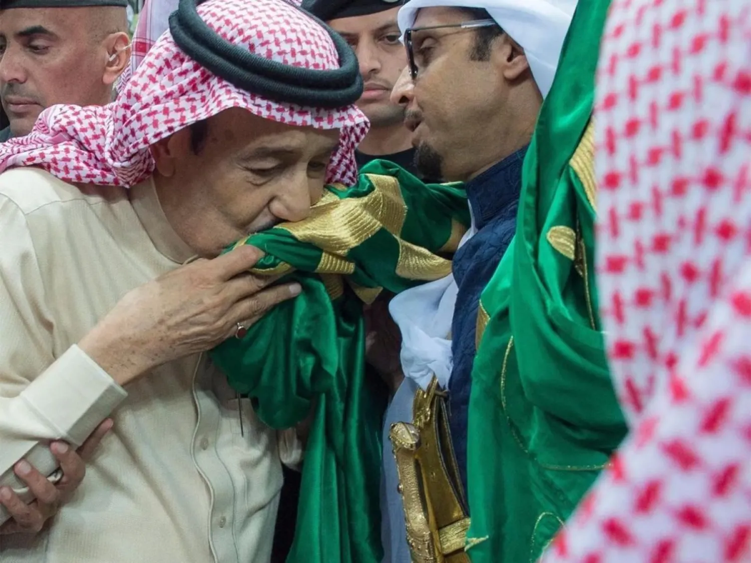 الملك سلمان مقبّلاً العلم السعودي (واس)