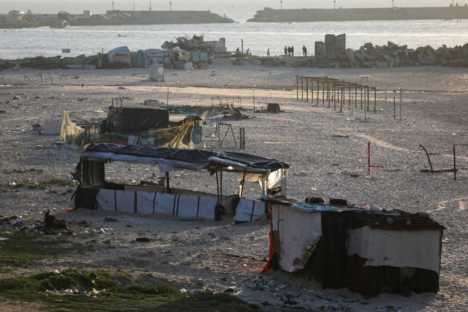 فلسطينيون يتجمعون على الشاطئ بالقرب من الملاجئ التي تضررت خلال الهجوم الإسرائيلي في مدينة غزة (رويترز)