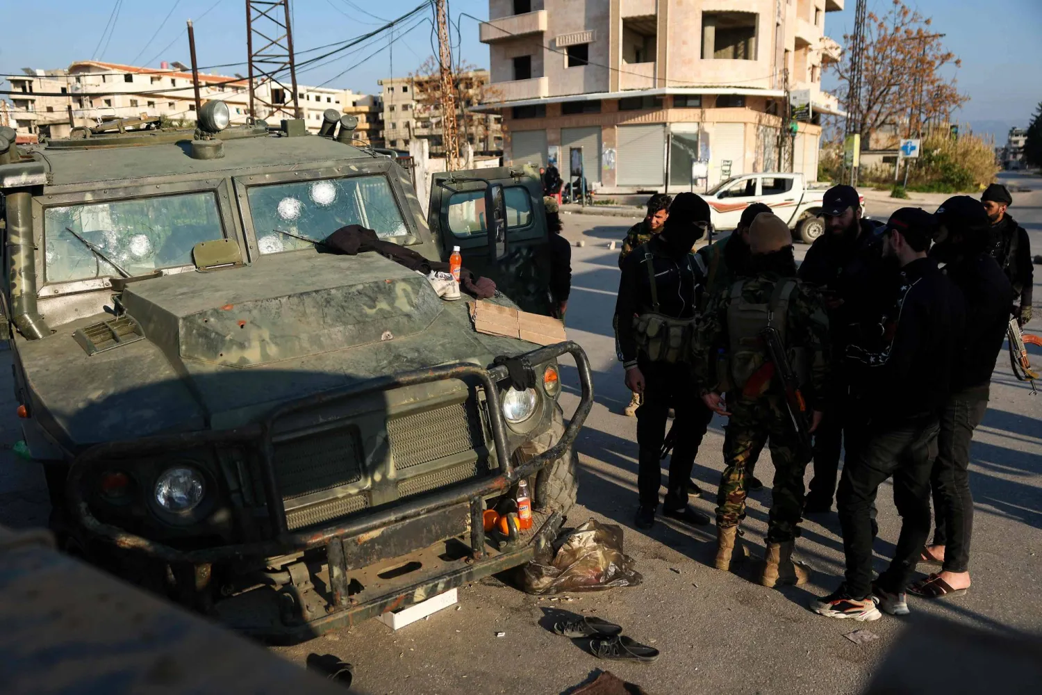 عناصر من قوات الأمن الموالية للحكومة السورية المؤقتة يقفون بجوار مركبة عسكرية متضررة كان يسيطر عليها أنصار الرئيس المخلوع بشار الأسد في بلدة حميميم في محافظة اللاذقية الساحلية بسوريا 11 مارس 2025 (أ.ف.ب)