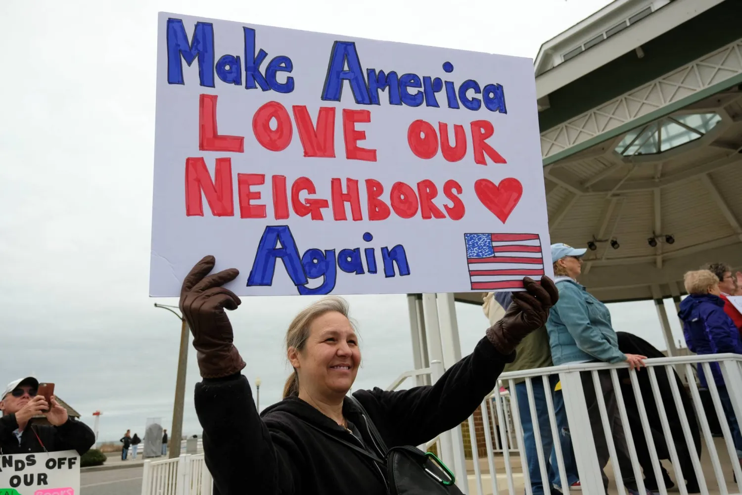 متظاهرة تحمل لافتة «لنجعل أميركا تحب جيرانها مرة أخرى» خلال الاحتجاج ضد ترمب في ولاية ديلاوير (رويترز)