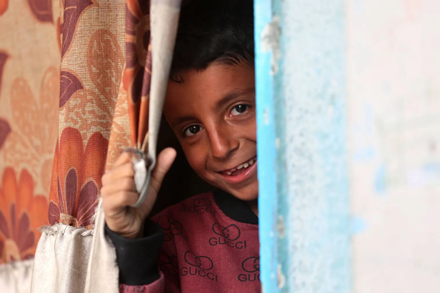 طفل فلسطيني يبتسم وهو يطل من داخل ملجأ في مدينة غزة (أ.ف.ب)