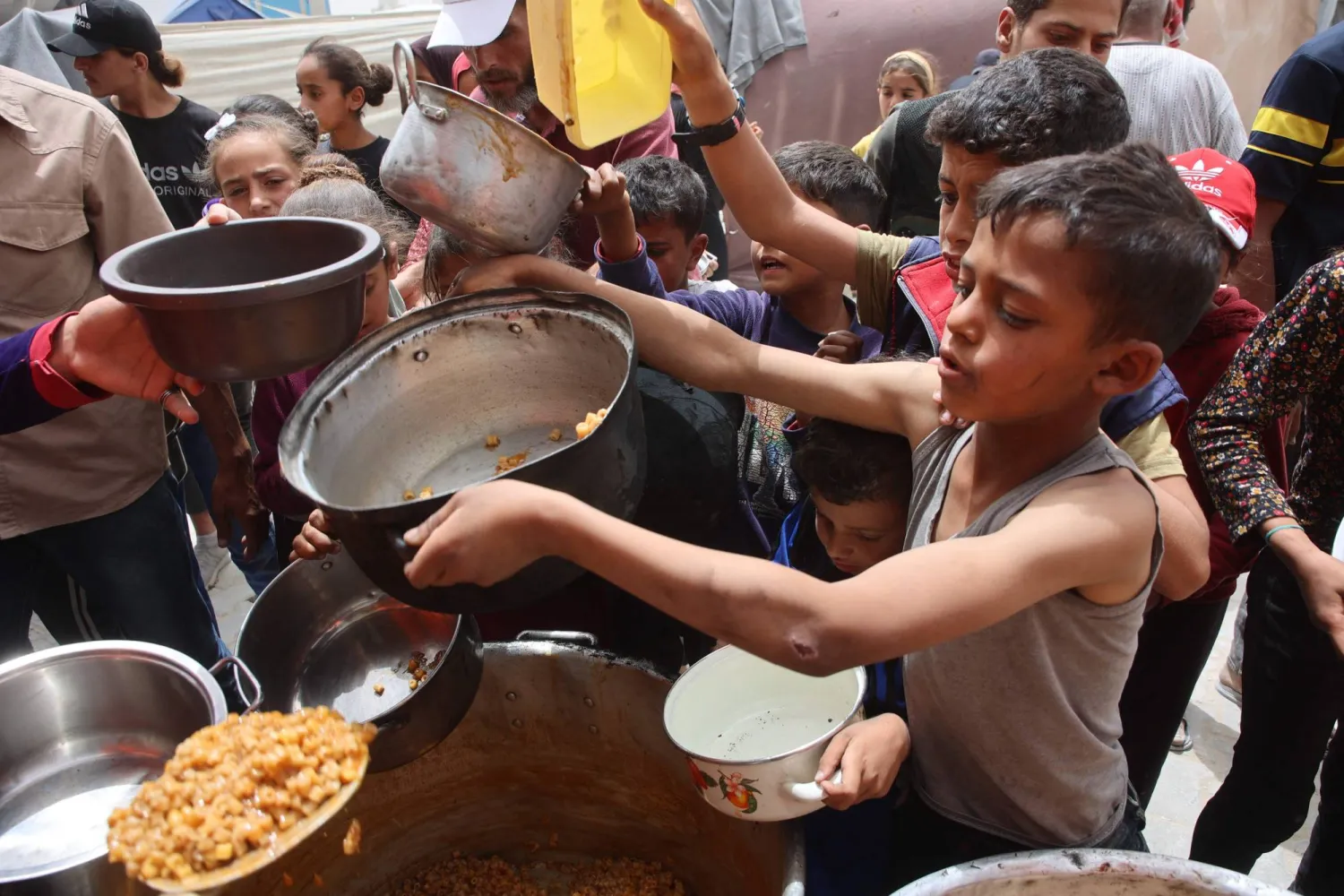طفل فلسطيني يحمل إناء ويحاول الحصول على حصة طعام من أحد المطابخ الخيرية بمدينة غزة (أ.ف.ب)