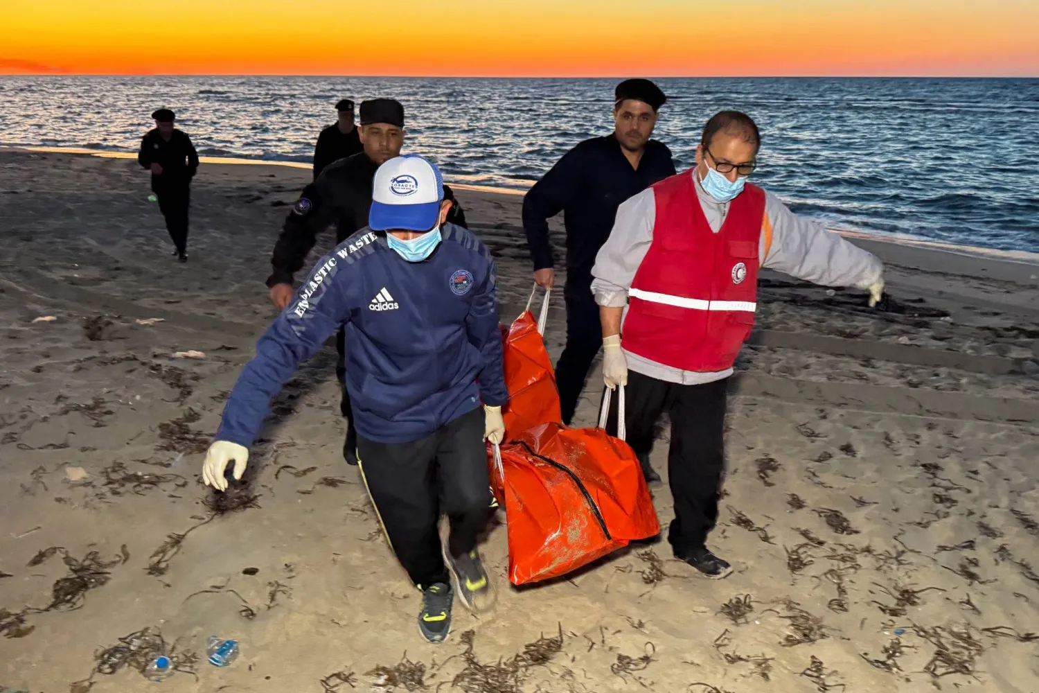 عناصر من الهلال الأحمر الليبي يحملون جثة مهاجر في حقيبة بعد العثور عليها على شاطئ مصراتة (رويترز)