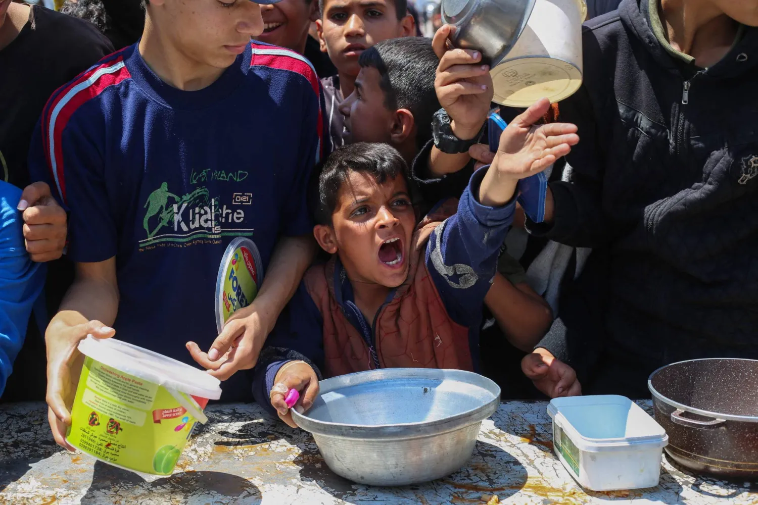 صبي فلسطيني مع أقرانه يحاول الحصول على الطعام من مطبخ خيري في مخيم النصيرات وسط غزة يوم الاثنين (أ.ف.ب)