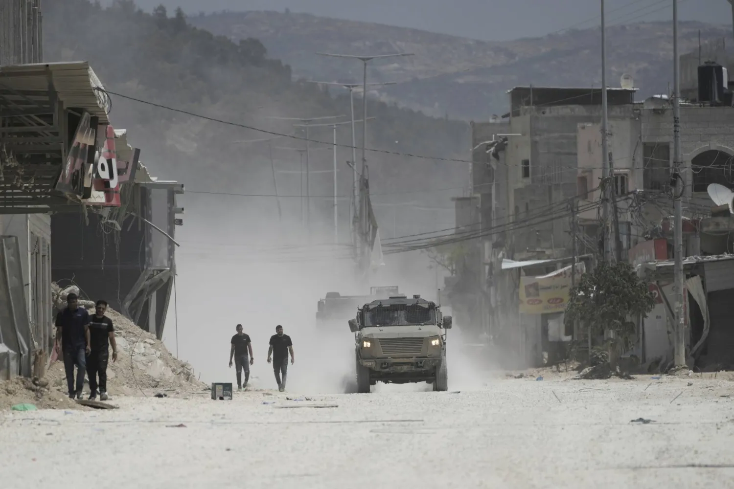 سكان بمخيم نور شمس للاجئين في الضفة الغربية يسيرون إلى جانب مركبات الجيش الإسرائيلي بينما يخلي الناس منازلهم (أ.ب) 