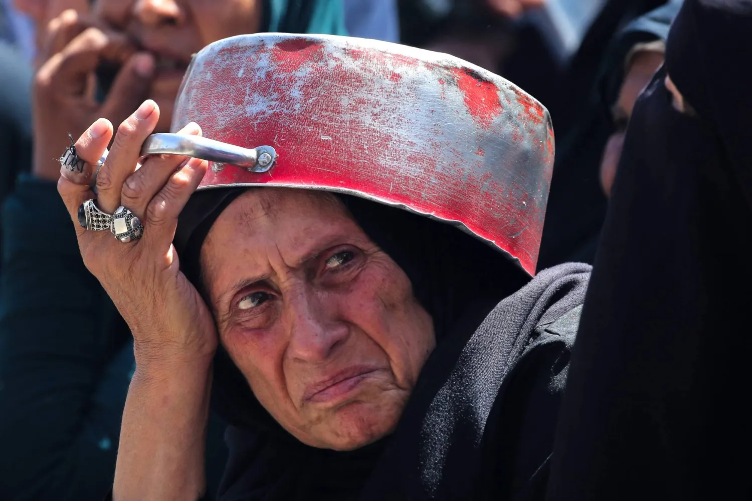 سيدة فلسطينية تستخدم وعاء لحمايتها من الشمس خلال انتظارها الحصول على طعام في نقطة توزيع بمخيم النصيرات وسط قطاع غزة (أ.ف.ب)