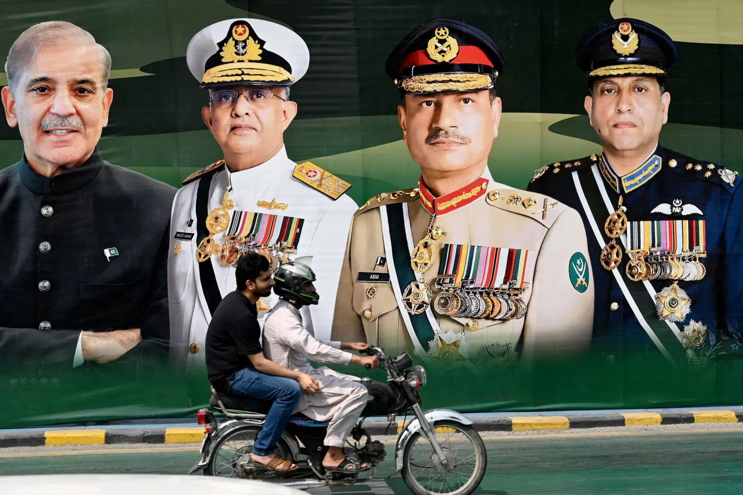 ركاب يمرون أمام لوحة إعلانية عليها صور رئيس الوزراء الباكستاني شهباز شريف (يسار) ورئيس البحرية الأدميرال نافيد أشرف (الثاني يسار) ورئيس أركان الجيش الجنرال سيد عاصم منير (الثاني يمين) ورئيس أركان القوات الجوية المارشال ظهير أحمد بابر معروضة على طول شارع في لاهور في 24 مايو 2025 (أ.ف.ب)