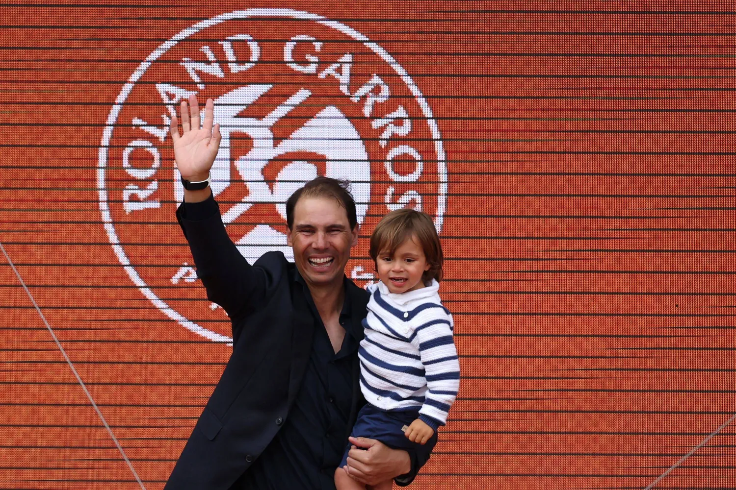 Former Spanish player Rafael Nadal, with his son Rafa junior in his arms, greets the spectators at the end of a ceremony honoring his career on Court Philippe-Chatrier during the French Open tennis tournament at the Roland-Garros Complex in Paris on May 25, 2025. (Photo by Franck FIFE / AFP)