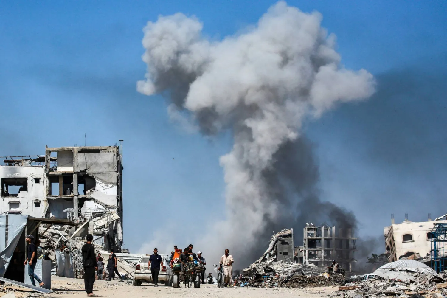 People  move past destroyed buildings as smoke billows following an Israeli strike in Jabalia, in the northern Gaza Strip on May 25, 2025. (Photo by Bashar TALEB / AFP)