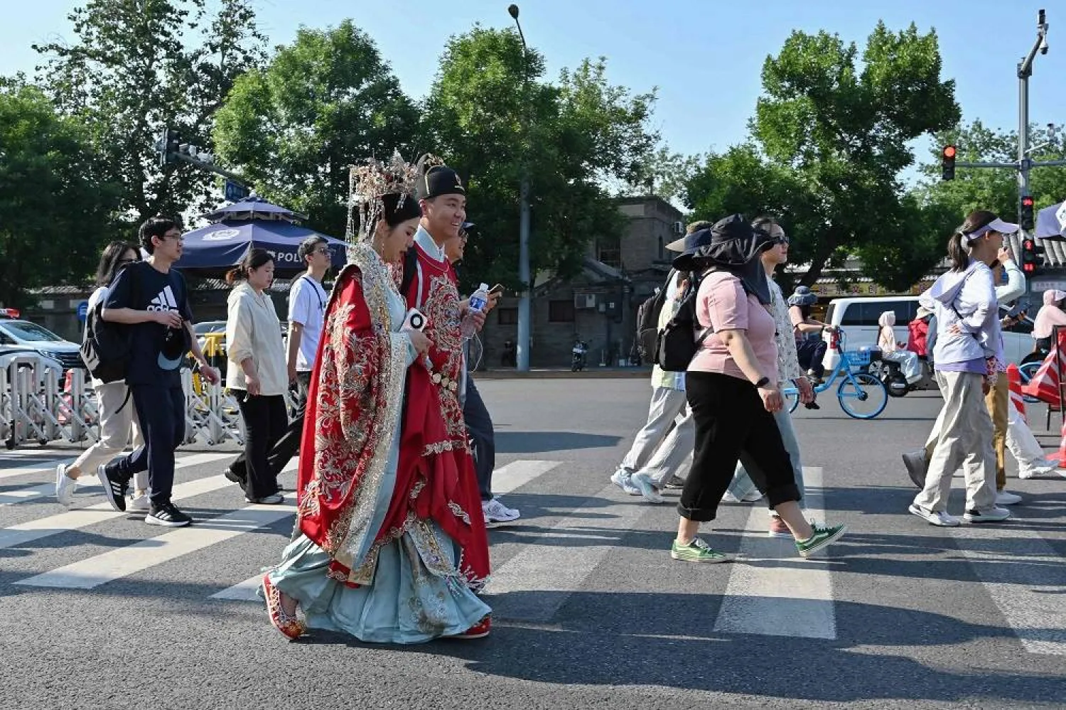 A couple in traditional costumes walk on a pedestrian crossing for a wedding photo shoot at the Forbidden City in Beijing on May 24, 2025. (AFP)