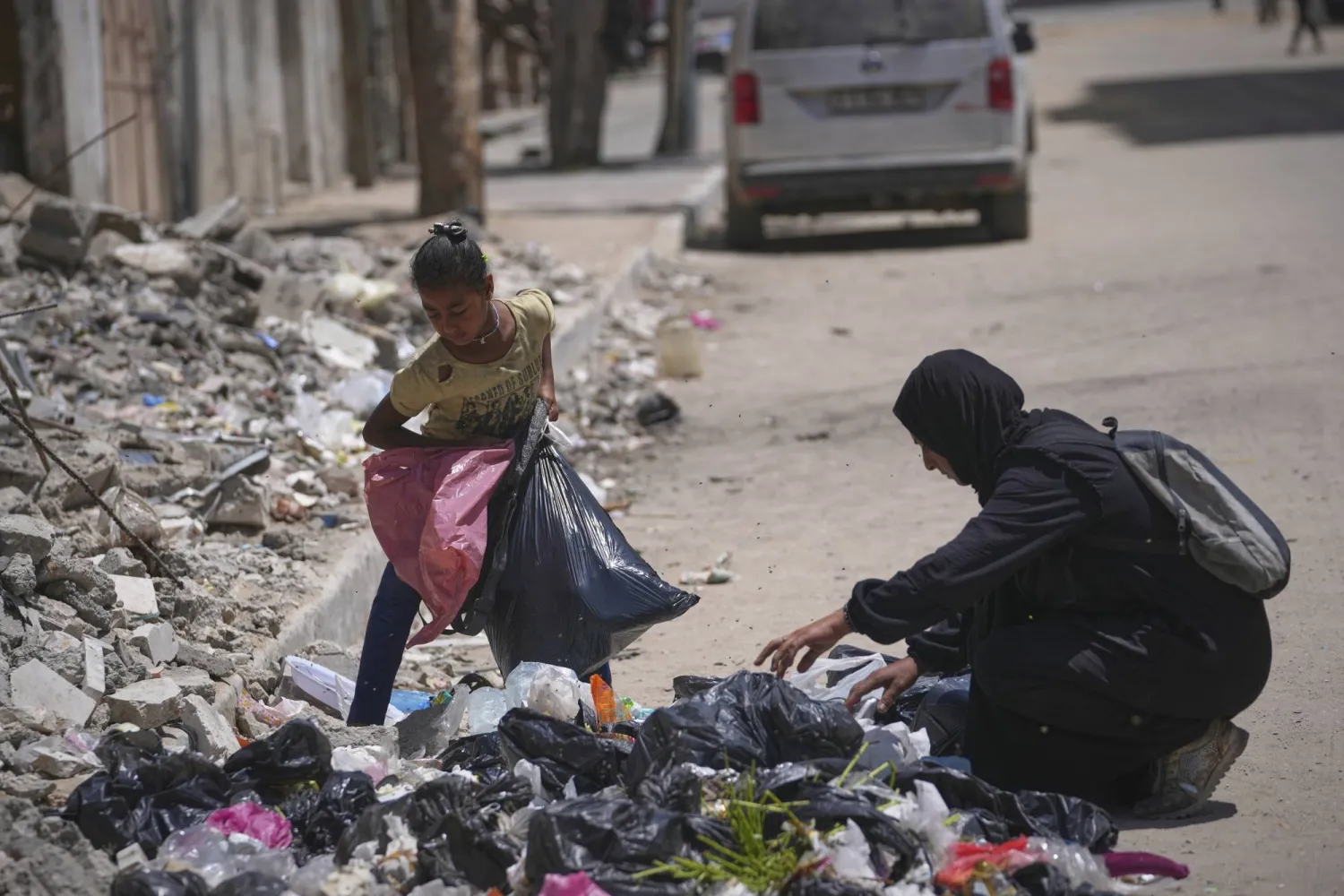 السيدة الفلسطينية إسلام أبو طعيمة تبحث مع طفلتها وعد عن أي طعام في القمامة (أ.ب)