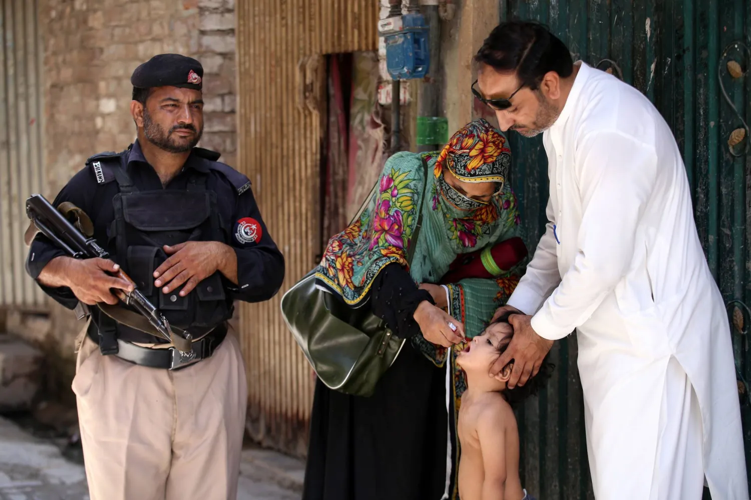 ضابط شرطة يراقب طفلاً يتلقى قطرات لقاح شلل الأطفال خلال حملة تطعيم من منزل إلى منزل في بيشاور - مقاطعة خيبر بختونخوا - باكستان - 26 مايو 2025. وأطلق رئيس الوزراء الباكستاني الحملة الوطنية الثالثة للتطعيم ضد شلل الأطفال في البلاد عام 2025 والتي تستمر من 26 إلى 31 مايو بهدف تطعيم أكثر من 45 مليون طفل (إ.ب.أ)