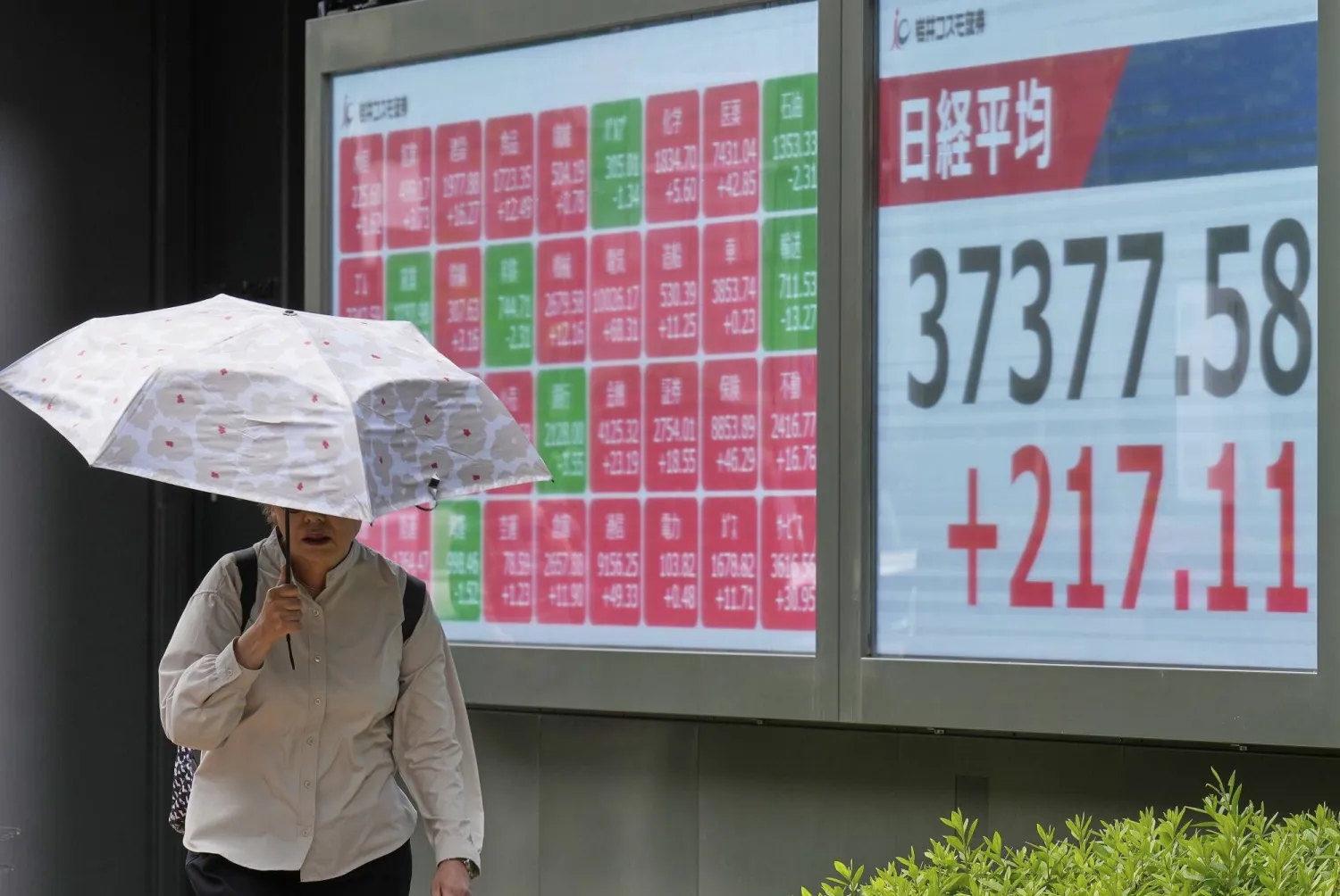 سيدة تمر أمام لوحة إلكترونية تعرض حركة الأسهم في السوق اليابانية بوسط العاصمة طوكيو (أ.ب)