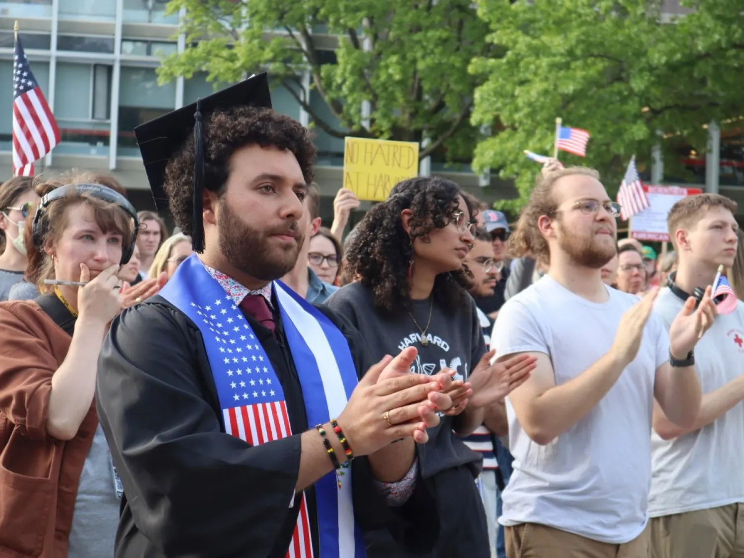 شخص يرتدي وشاحاً عليه علمَي الولايات المتحدة والسلفادور خلال مشاركته في مسيرة «هارفارد تقف موحدة» احتفاء بالطلاب الدوليين في الجامعة (أ.ب)
