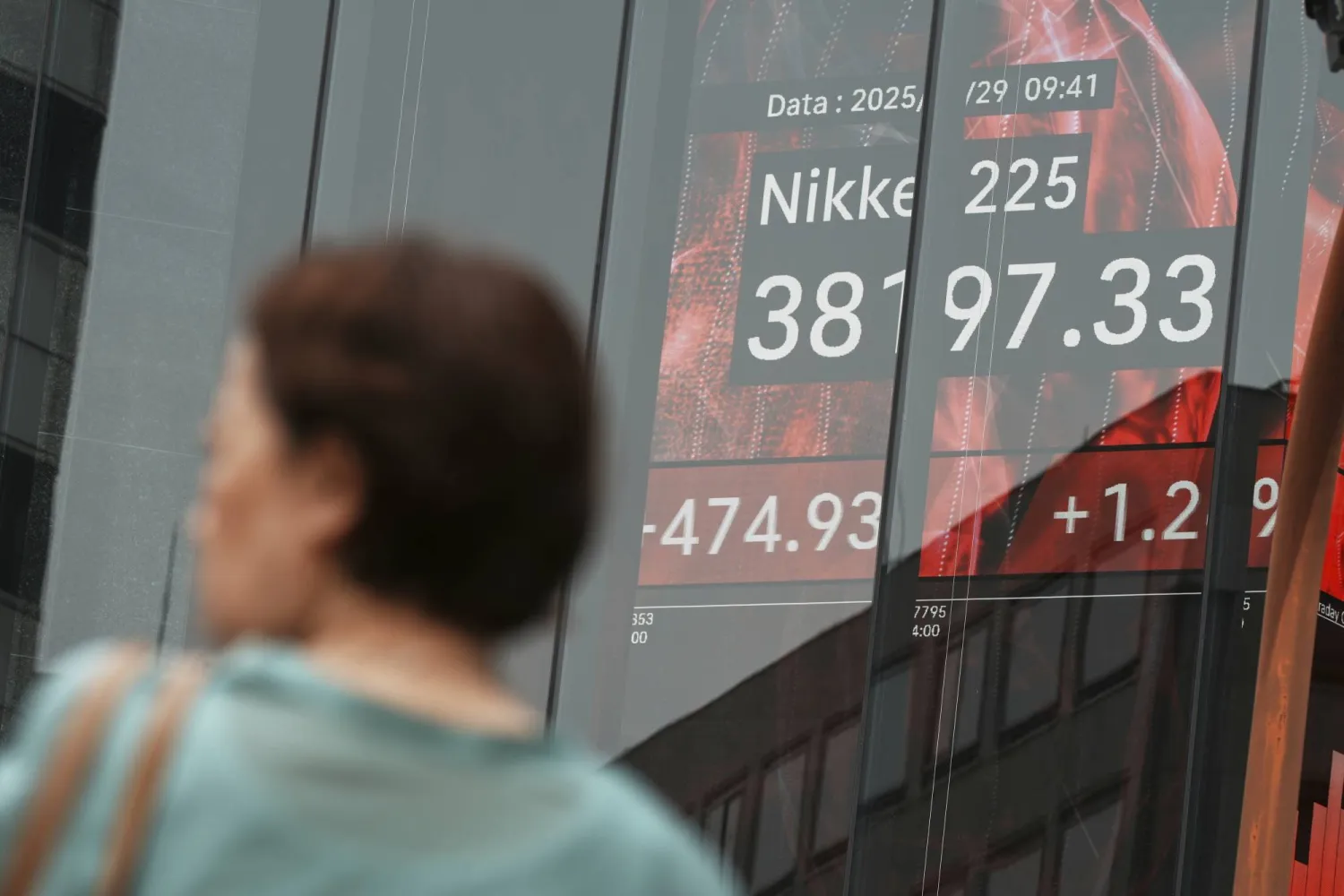 شخص يمر أمام لوحة تعرض مؤشر نيكي في طوكيو (أ.ب)