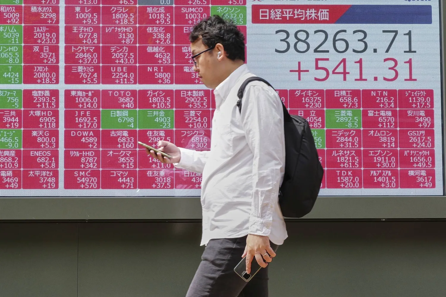 رجل يسير أمام لوحة تعرض حركة الأسهم وسط طوكيو (أ.ب)