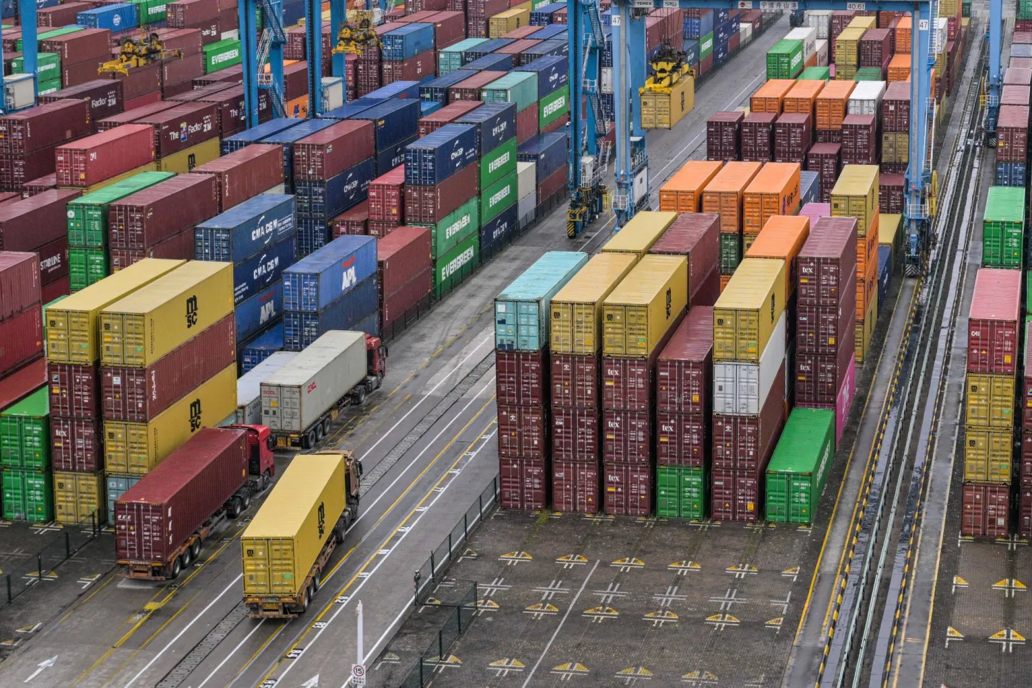 شاحنات تمر بين آلاف الحاويات المعدة للتصدير في ميناء نينغبو شرق الصين (أ.ف.ب)