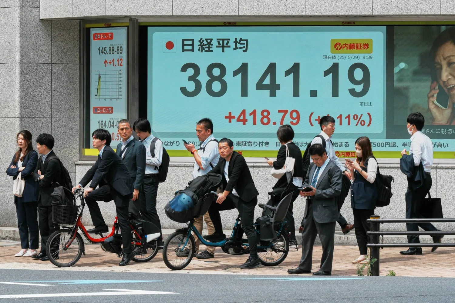 مشاة في أحد شوارع العاصمة اليابانية طوكيو يمرون أمام لوحة إلكترونية تعرض حركة الأسهم (أ.ب)