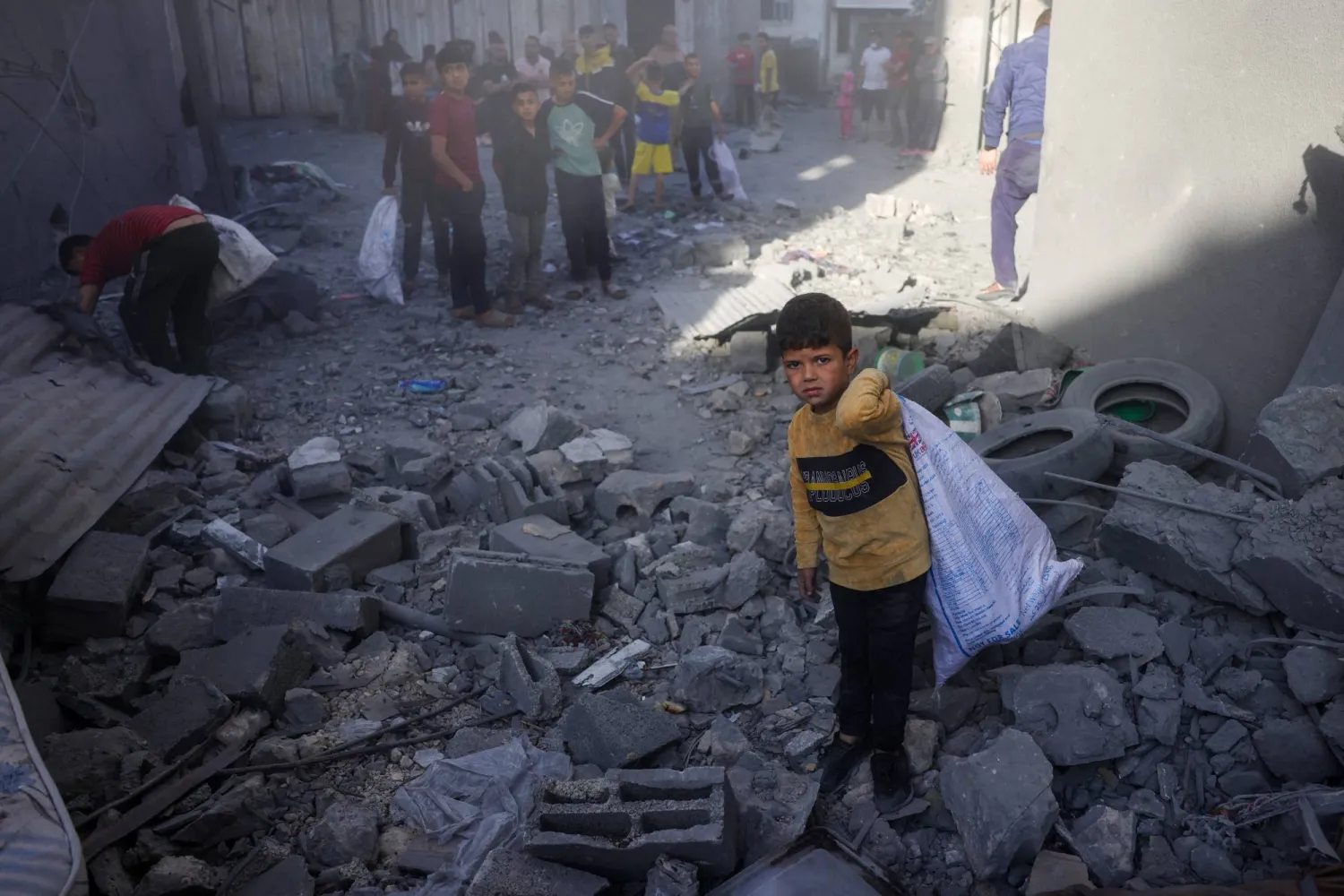 أطفال يجمعون أغراضهم بينما يتفقد فلسطينيون موقع غارة إسرائيلية ليلية بجباليا وسط قطاع غزة (أ.ف.ب)