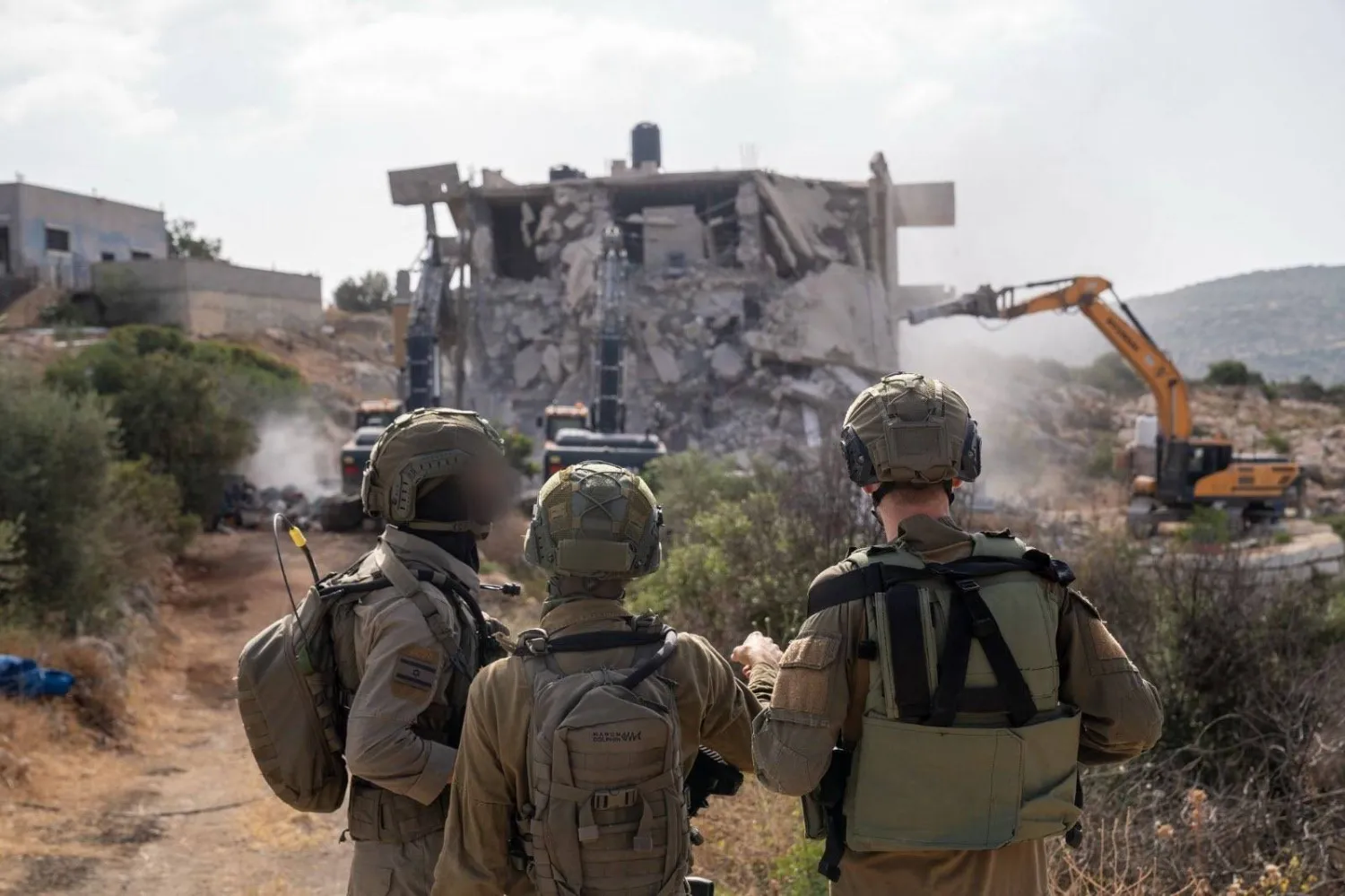 جنود إسرائيليون يشاهدون آلية ثقيلة تهدم منزلاً في الضفة الغربية (الجيش الإسرائيلي)