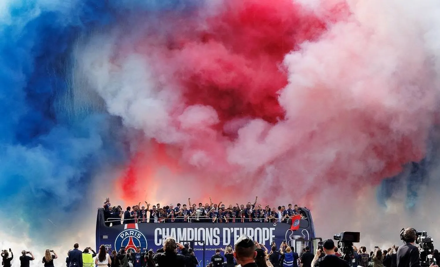 PSG team and staff celebrate under smoke colored in the French national colors during an open-top bus parade of the team on the Champs Elysee boulevard in Paris, France, 01 June 2025. (EPA)