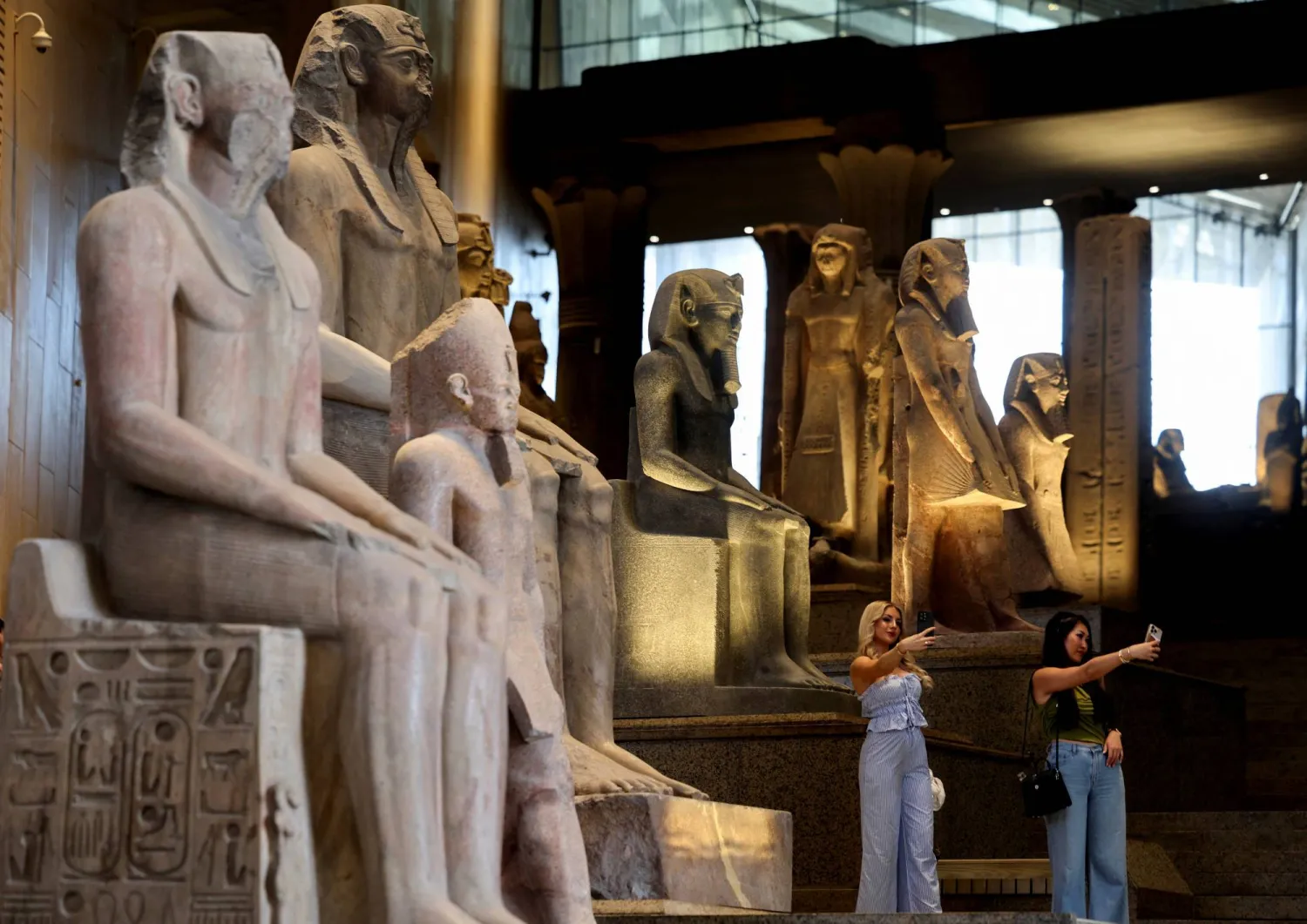 سياح يقفون بجوار المعروضات المتحفية المعروضة في المتحف المصري الكبير (رويترز)