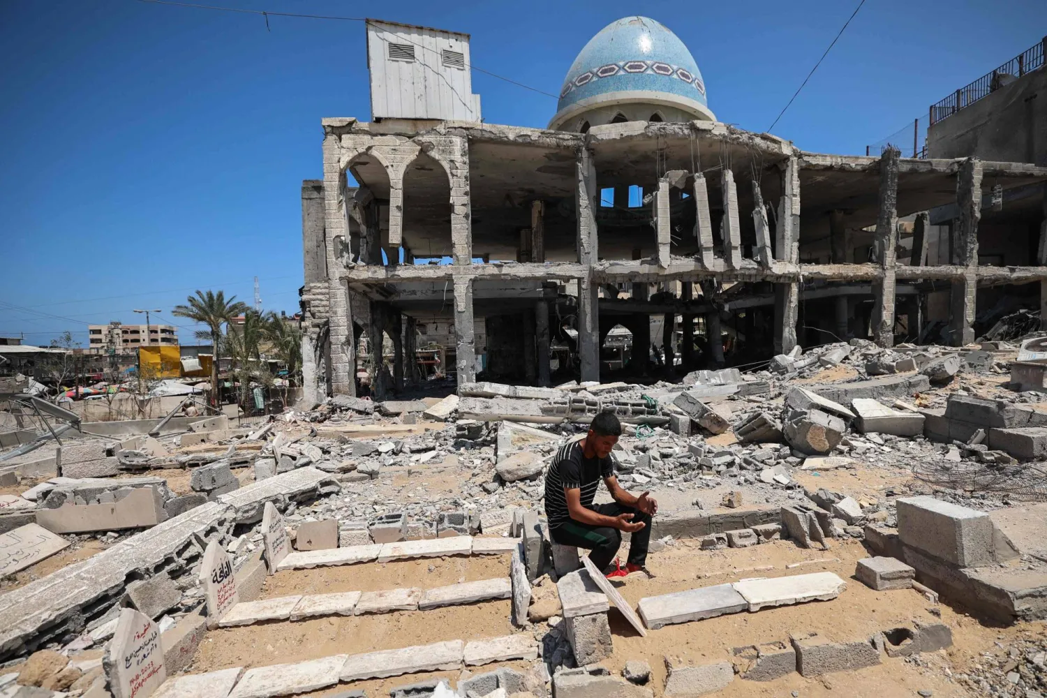 فلسطيني يقرأ الفاتحة عند قبر دمرته ضربة إسرائيلية أصابت أيضاً مسجد الأنصار في دير البلد بوسط قطاع غزة يوم الثلاثاء (أ.ف.ب)