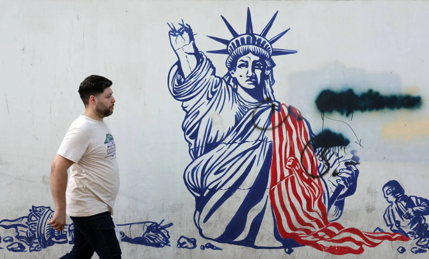 رجل إيراني يمر أمام جدارية مناهضة للولايات المتحدة بجانب السفارة الأميركية في طهران (إ.ب.أ)