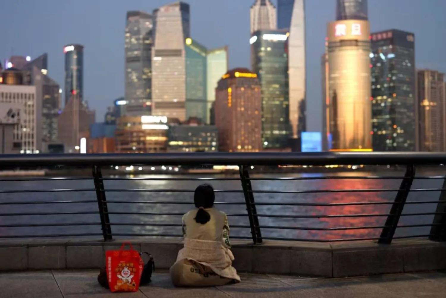 امرأة تجلس على جسر البوند وتطل على حي بودونغ المالي في شنغهاي (رويترز)