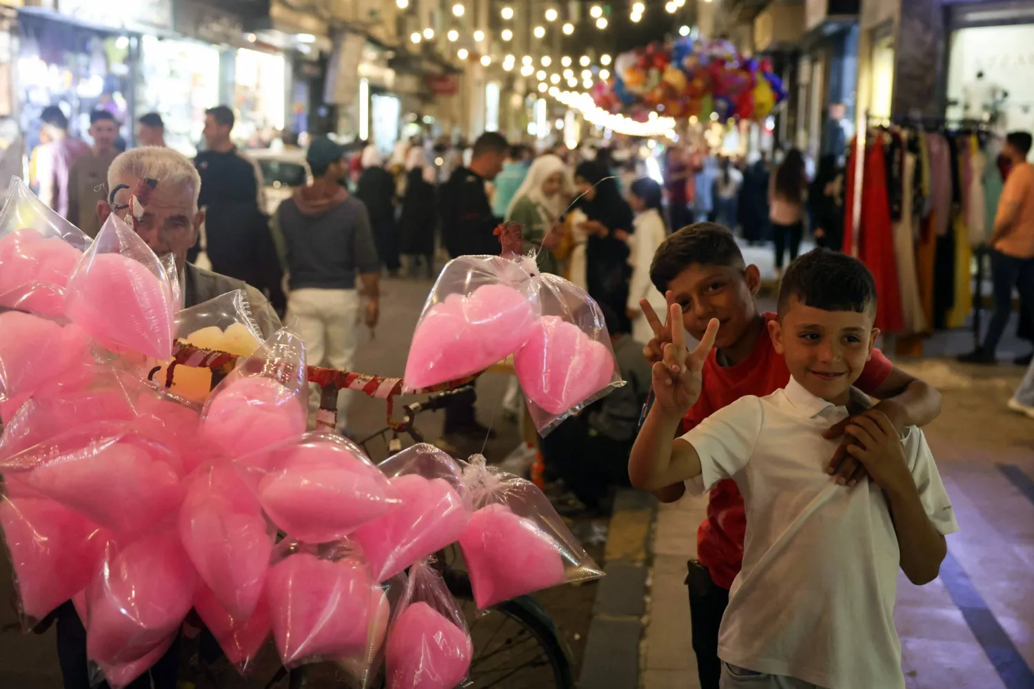 أطفال يمرحون وسط سوق يعج بالمتسوقين والبضائع قبيل عيد الأضحى في مدينة حمص السورية (أ ف ب)