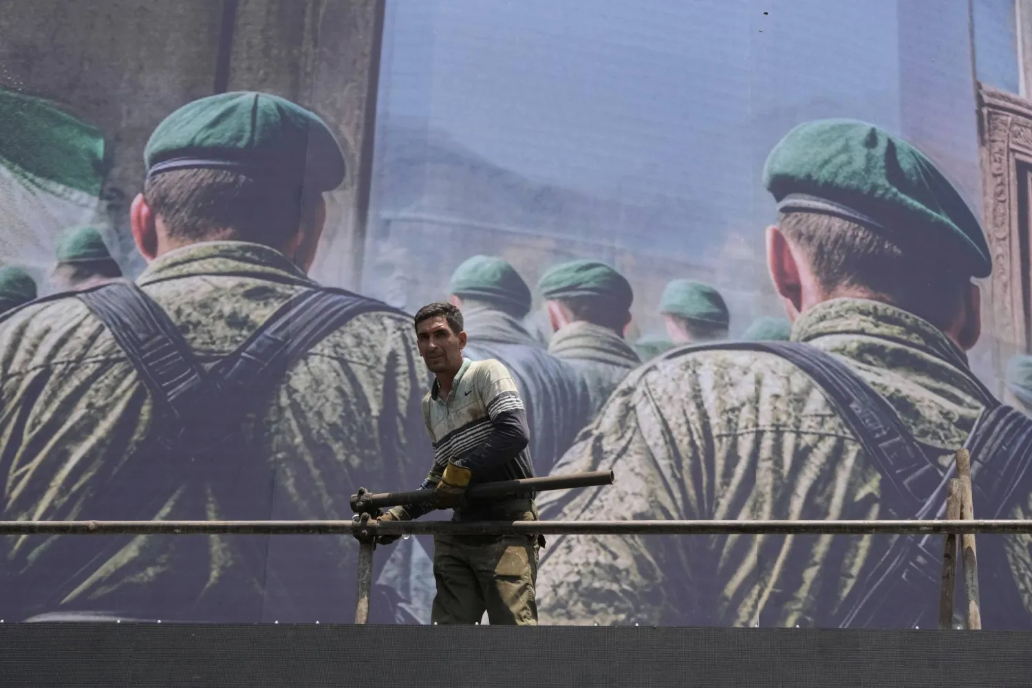 عامل يقف أمام لافتة تُصور جنوداً إيرانيين في طريقهم لمهاجمة أراضٍ إسرائيلية في ساحة انقلاب (الثورة) وسط طهران (أ.ب)