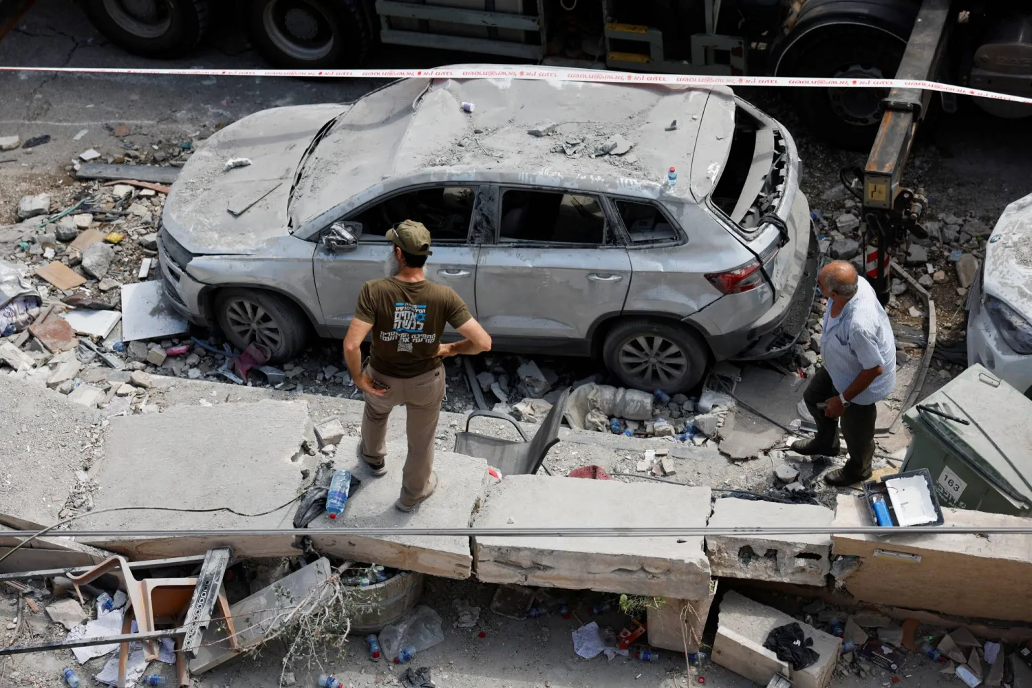 أشخاص يقفون بجوار مركبة متضررة بعد أن أصابت صواريخ أُطلقت من إيران مبنى سكنياً في طمرة شمال إسرائيل (رويترز)