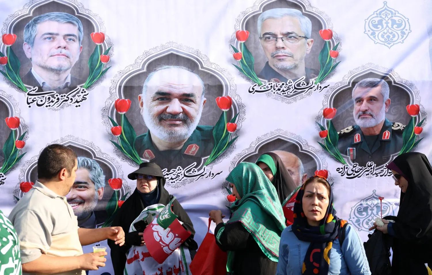 إيرانيون يقفون أمام لوحة تحمل صور قادة «الحرس الثوري» الإيراني الذين قُتلوا في الهجوم الإسرائيلي (إ.ب.أ)